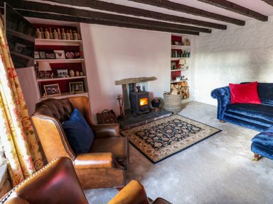 A living room with leather armchairs a blue sofa a wood burning stove and shelves with bottles and photos at Rose Hip Cottage in Bellingham