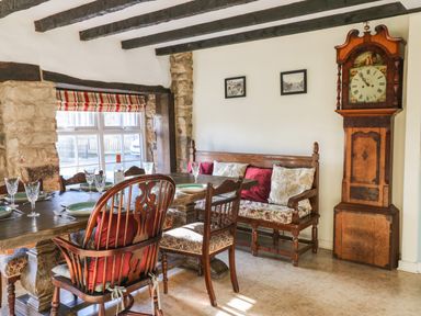 A dining room with a wooden table set with green plates and glasses wooden chairs a cushioned bench under a window with a stone frame and an antique grandfather clock on the wall at Rose Hip Cottage in Bellingham