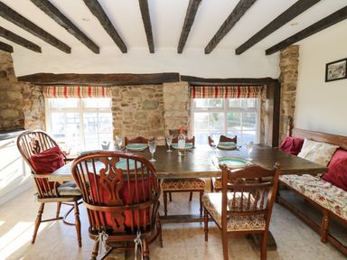 A dining area with wooden table and chairs by windows with stone walls and ceiling beams at Rose Hip Cottage in Bellingham
