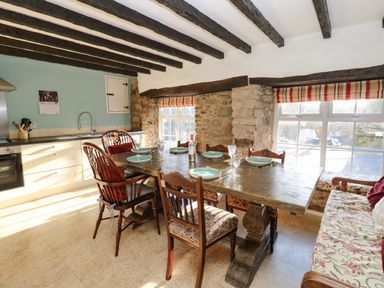 A dining area with a wooden table set with plates and glasses near windows with striped blinds in Rose Hip Cottage in Bellingham