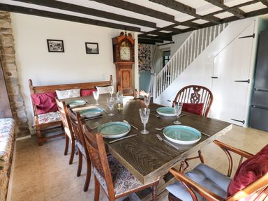 A dining area with a wooden table set for six and a wooden bench along a white wall with two pictures at Rose Hip Cottage in Bellingham