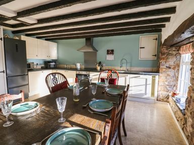 A kitchen with wooden table set for four with plates and glasses and white cabinets at Rose Hip Cottage in Bellingham