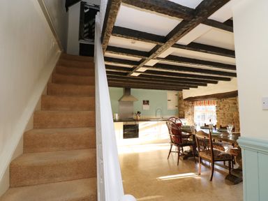 A kitchen and dining area with exposed wooden ceiling beams and a carpeted staircase at Rose Hip Cottage in Bellingham