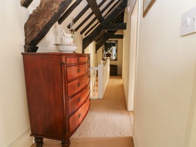 A narrow hallway with wooden beams on the ceiling a wooden chest of drawers a mirror on the wall and a carpeted floor at Rose Hip Cottage in Bellingham