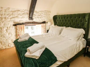 A bedroom with a green upholstered bed a white bedspread and rolled towels on the bed at Rose Hip Cottage in Bellingham