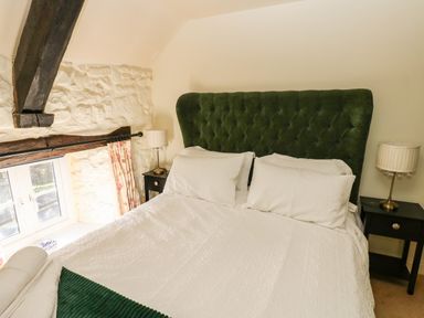 A bedroom with a bed with green headboard white bedding two bedside tables with lamps and a window with floral curtains at Rose Hip Cottage in Bellingham