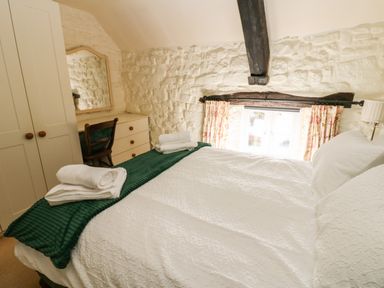 A bedroom with a large bed white bedding folded towels a dresser with a mirror wooden chair and floral curtains at Rose Hip Cottage in Bellingham