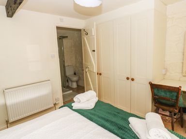 A bedroom with a bed and rolled towels next to a wardrobe and an open door to a bathroom at Rose Hip Cottage in Bellingham