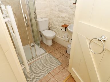 A small bathroom with a shower enclosure, toilet, sink, and tiled floor at Rose Hip Cottage in Bellingham