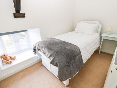 A small bedroom with a single bed a bedside table with a lamp a window with a teddy bear on the sill at Rose Hip Cottage in Bellingham