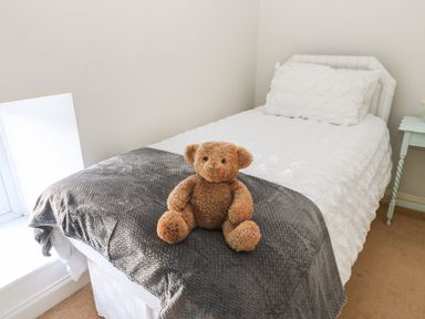 A single bed with white bedding a gray blanket and a teddy bear on top at Rose Hip Cottage in Bellingham