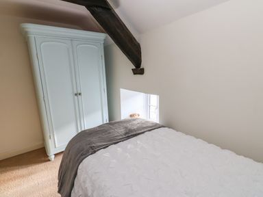 A bedroom with a white wardrobe a bed with white and gray bedding and a window with a teddy bear on the sill at Rose Hip Cottage in Bellingham