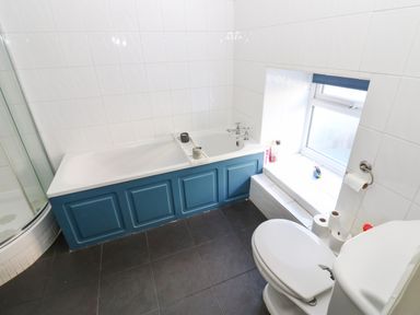 A bathroom with a bathtub blue paneling toilet window and shower at Rose Hip Cottage in Bellingham