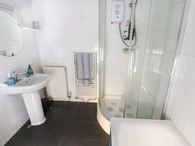 A bathroom with a pedestal sink mirror radiator towel rail and curved glass shower at Rose Hip Cottage in Bellingham