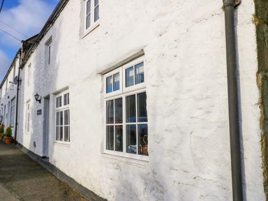 The exterior of a white stone building with multiple rectangular windows on a sidewalk at Rose Hip Cottage in Bellingham