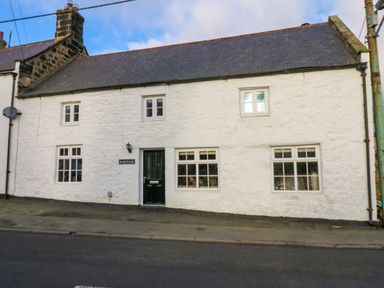 A white stone cottage with black door and multiple windows on a street at Rose Hip Cottage in Bellingham