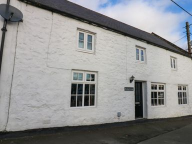 Exterior view of a white stone cottage with black door and multiple windows at Rose Hip Cottage in Bellingham