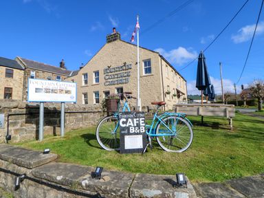 A bike with a cafe and b b sign on grass in front of a stone building and outdoor seating at Fountain Cottage in Bellingham