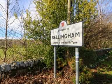 A welcome sign for Bellingham capital of the North Tyne beside a stone wall and trees in an outdoor rural setting
