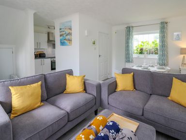A living room with two gray sofas with yellow pillows a small kitchen and a dining table by a window at Sea Rose in Aberporth