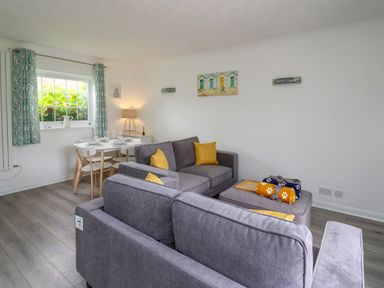 A living room with grey sofas yellow cushions a dining table with chairs and curtains at Sea Rose in Aberporth