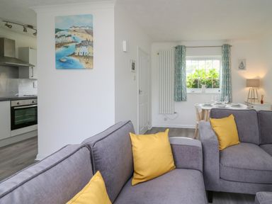 A living area with gray sofas and yellow cushions next to a dining table and kitchen at Sea Rose in Aberporth