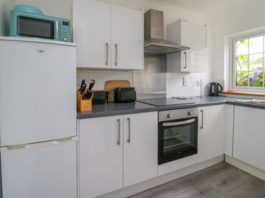 A kitchen with white cabinets a black countertop a refrigerator a microwave a knife block a toaster a kettle and a window at Sea Rose in Aberporth