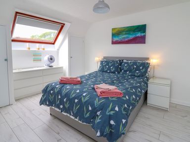 A bedroom with a bed covered in floral bedding bedside tables with lamps a dresser a fan and a skylight window at Sea Rose in Aberporth