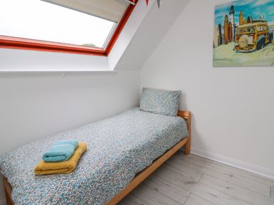 A single bed with patterned bedding and folded towels under a skylight window with a surfboard painting on the wall at Sea Rose in Aberporth