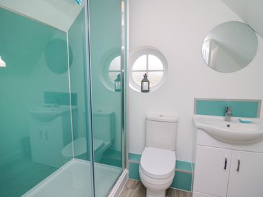 A bathroom with a shower enclosure a toilet a sink with cabinet and a round window at Sea Rose in Aberporth