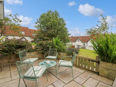 An outdoor patio with a set of green metal chairs and a table set with a teapot and cups next to a garden with shrubs and a tree at Sea Rose in Aberporth