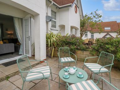 An outdoor patio area with metal chairs and a table set with a teapot and cups outside a white house with plants and shrubs at Sea Rose in Aberporth