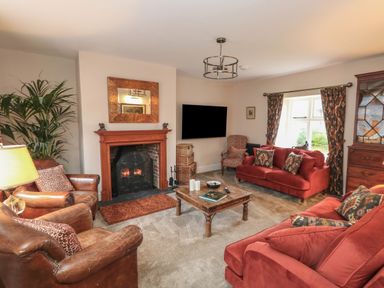 A living room with a fireplace red sofas leather armchairs a wooden coffee table and a television at Manor Farm House in Bere Regis
