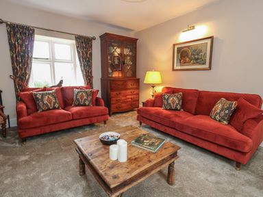 A living room with red sofas a wooden coffee table a wooden cabinet and patterned curtains at Manor Farm House in Bere Regis