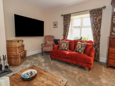 A living room with a red sofa cushions patterned chair a wooden coffee table and a wall mounted television at Manor Farm House Bere Regis