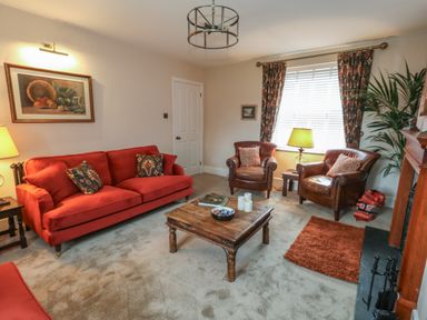 A living room with a red sofa two leather armchairs a wooden coffee table and a window with floral curtains at Manor Farm House in Bere Regis