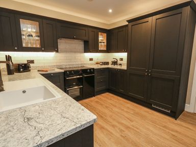 A kitchen with dark cabinets a white sink granite countertops and wooden flooring at Manor Farm House in Bere Regis