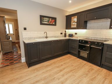 A kitchen with dark cabinets a black oven white countertop and wooden floor at Manor Farm House Bere Regis