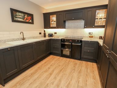 A kitchen with dark cabinets a sink an oven and wooden floor at Manor Farm House in Bere Regis