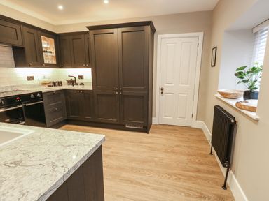 A kitchen with dark cabinets a marble countertop a white door a black radiator and a window with plants at Manor Farm House in Bere Regis
