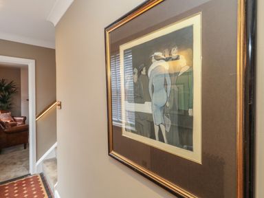 A hallway with a framed painting on the wall and a view into a living room with a leather armchair at Manor Farm House in Bere Regis