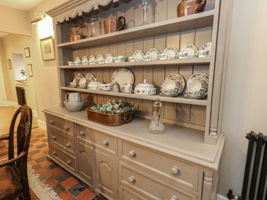 A wooden dresser with shelves holding glassware copper pots and patterned plates in a dining area at Manor Farm House in Bere Regis