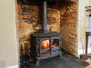 A wood burning stove in a brick fireplace with fireplace tools to the side at Manor Farm House in Bere Regis