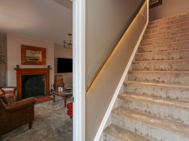 A carpeted staircase next to a living room with a fireplace TV and leather armchairs at Manor Farm House in Bere Regis