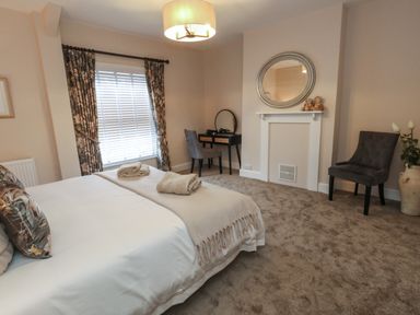 A bedroom with a bed and towels on it a desk and chair a mirror above a fireplace and another chair with a vase of flowers at Manor Farm House in Bere Regis