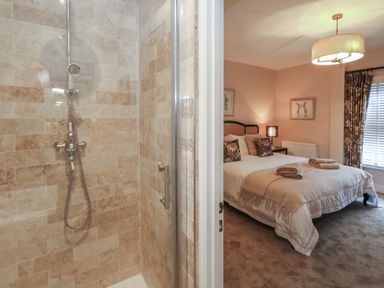 A bathroom shower with beige tiles next to a bedroom with a bed and rolled towels at Manor Farm House in Bere Regis