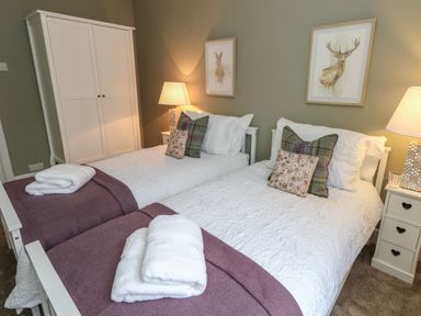 A bedroom with two beds white bedding and purple throws with a wardrobe and bedside tables with lamps at Manor Farm House in Bere Regis
