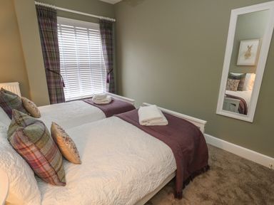 A bedroom with two single beds with pillows and folded towels by a window with curtains and a wall mirror at Manor Farm House Bere Regis