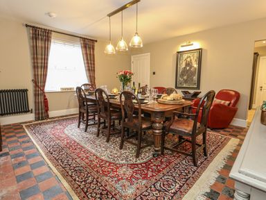 A dining room with a wooden table set with plates and glasses and patterned rug at Manor Farm House in Bere Regis