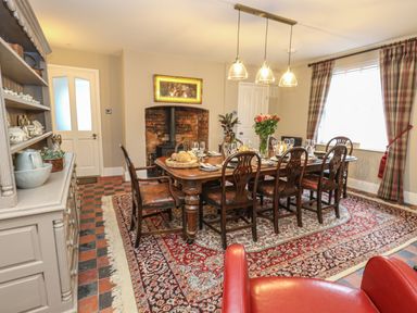A dining room with a wooden table set with glassware and bread near a fireplace and window at Manor Farm House in Bere Regis